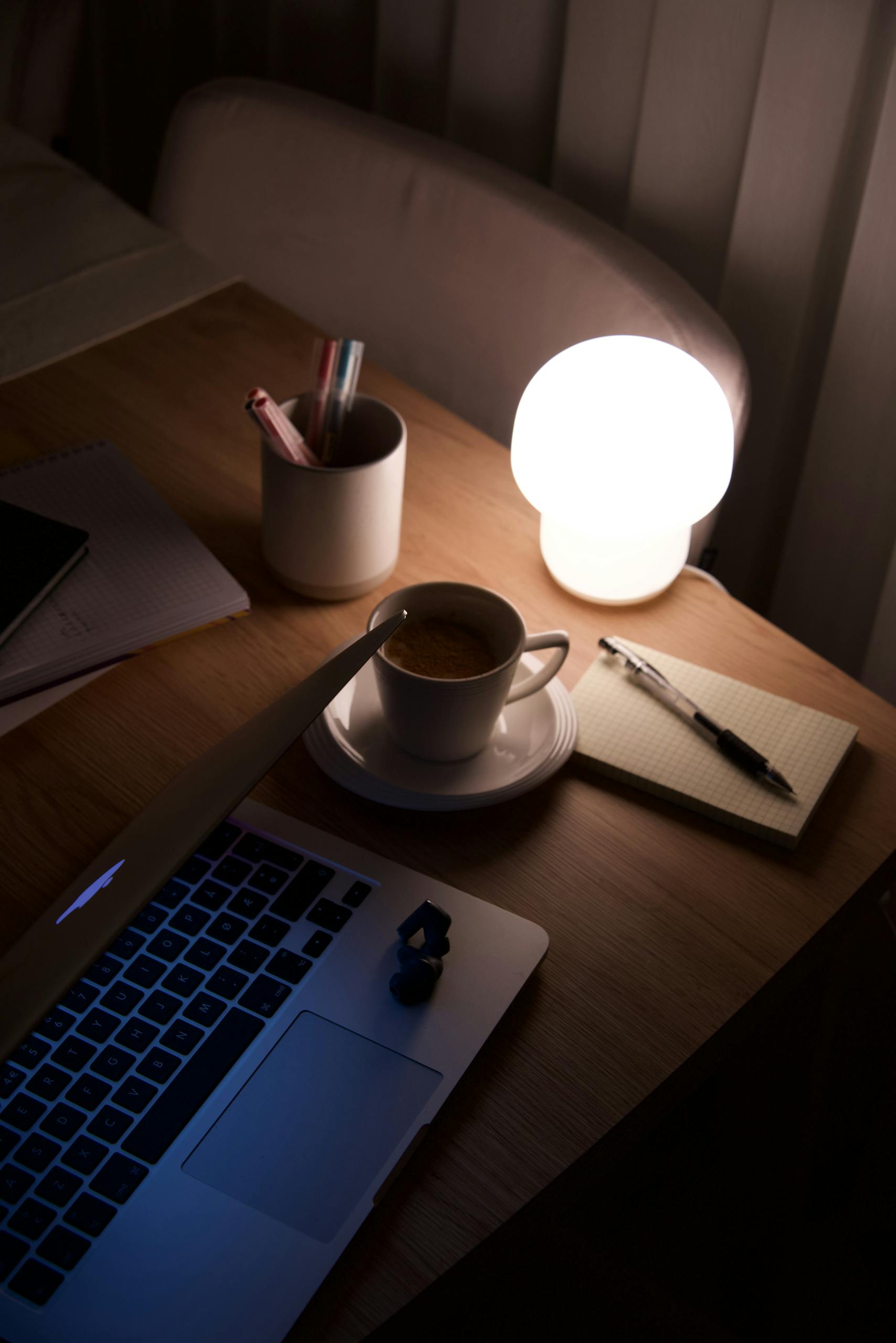 Warm workspace with a glowing lamp and coffee beside a laptop, perfect for late-night work.
